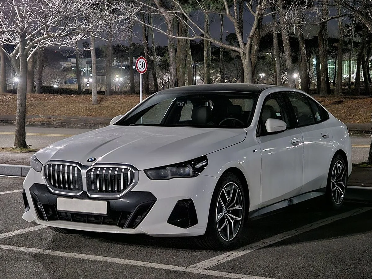 야간 공원 주차장에 세워 둔 흰색 BMW 5시리즈 G60 세단의 전면 3/4