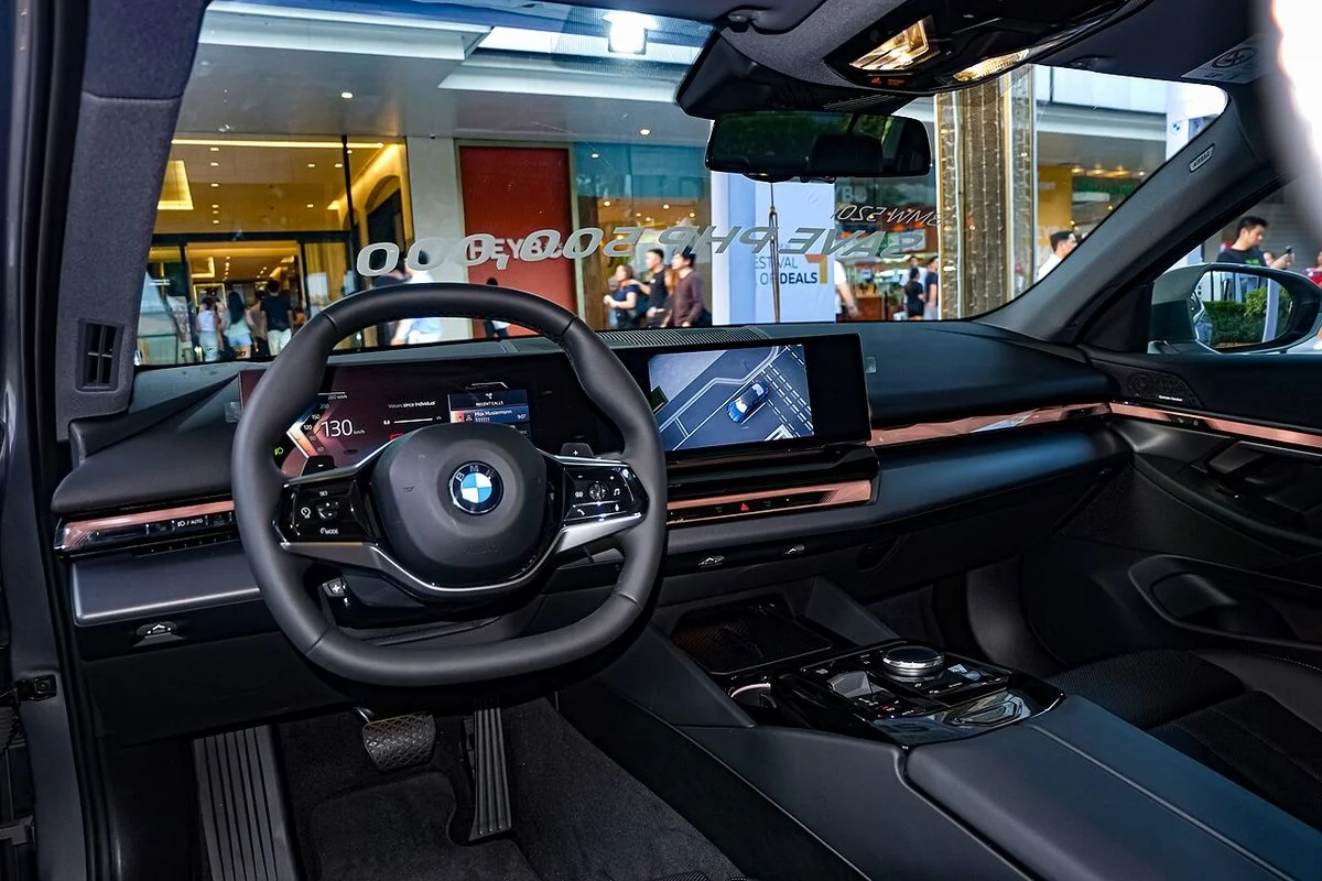 BMW 5시리즈 G60 520i의 운전석 실내, 스티어링 휠 너머로 이어진 커브드 디스플레이와 센터 콘솔이 보인다