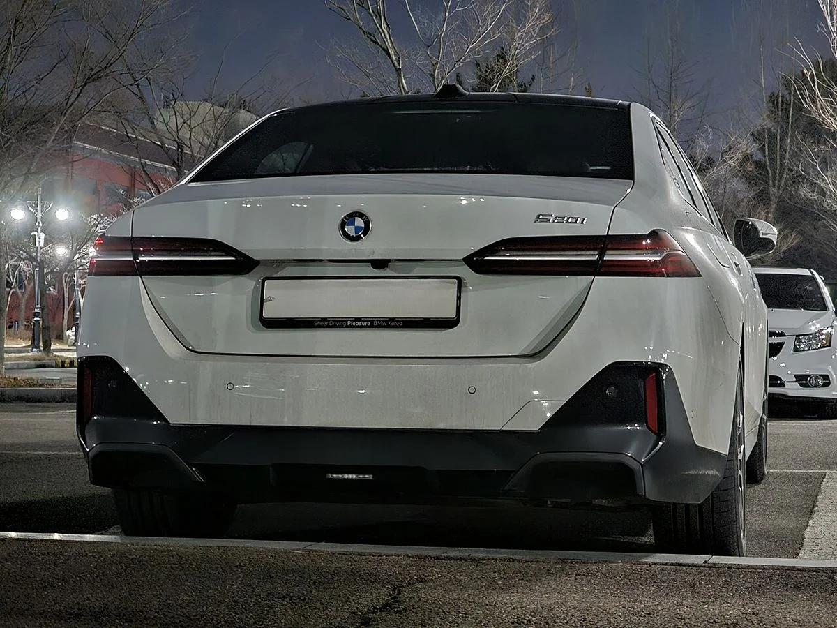 야간 주차장에 세워 둔 흰색 BMW 5시리즈 G60의 후면, 일자형 테일램프와 트렁크 리드가 보인다