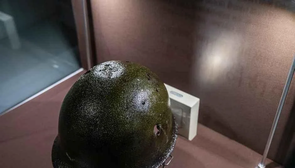 어두운 배경 속 진열장 안에 놓인 이끼색 철모 유물
