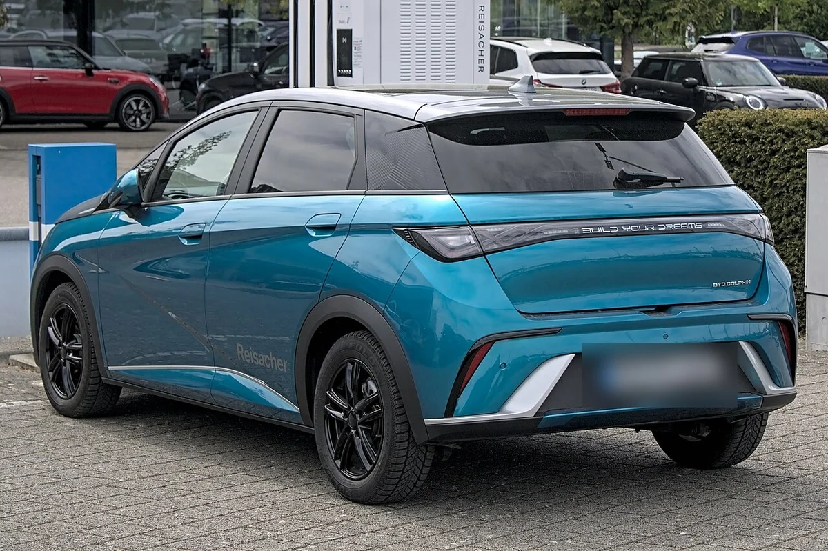청록색 BYD 돌핀의 후측면, 뒤쪽에 충전기가 서 있고 검은 후면 범퍼 하단이 보인다