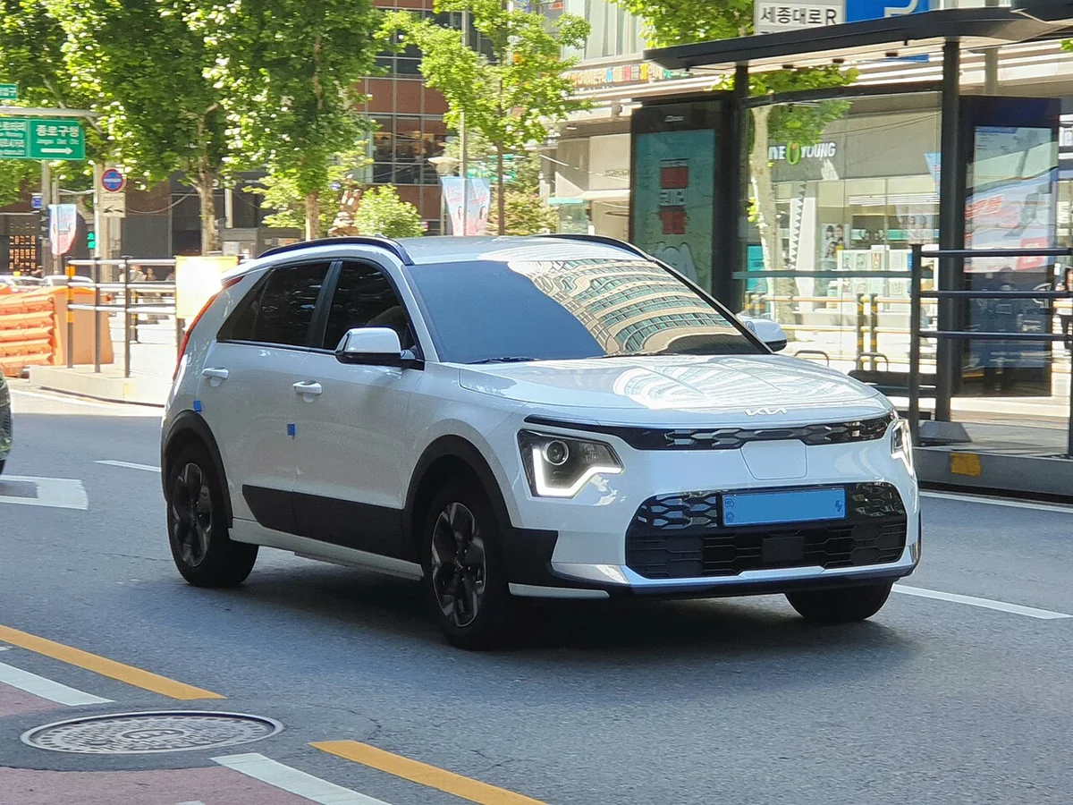 도로에 서 있는 흰색 기아 니로 EV 앞쪽에 전기차 파란 번호판이 붙어 있는 모습