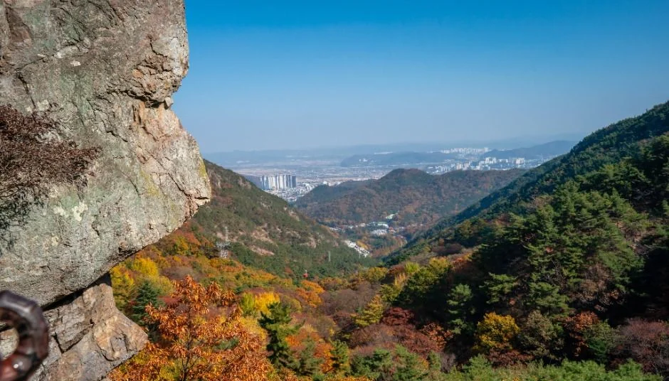 바위 절벽 옆으로 단풍 든 산과 먼 평지가 보이는 풍경
