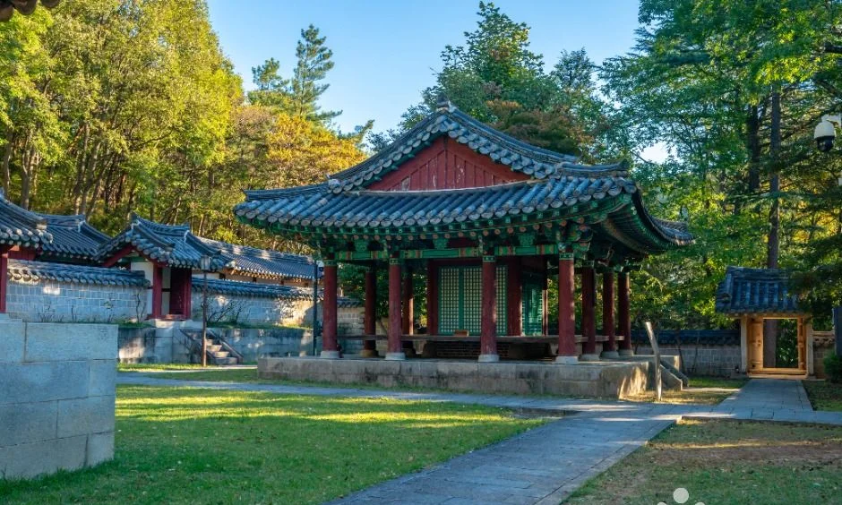 푸른 잔디와 담장 옆에 선 붉은 기둥의 채미정 정자