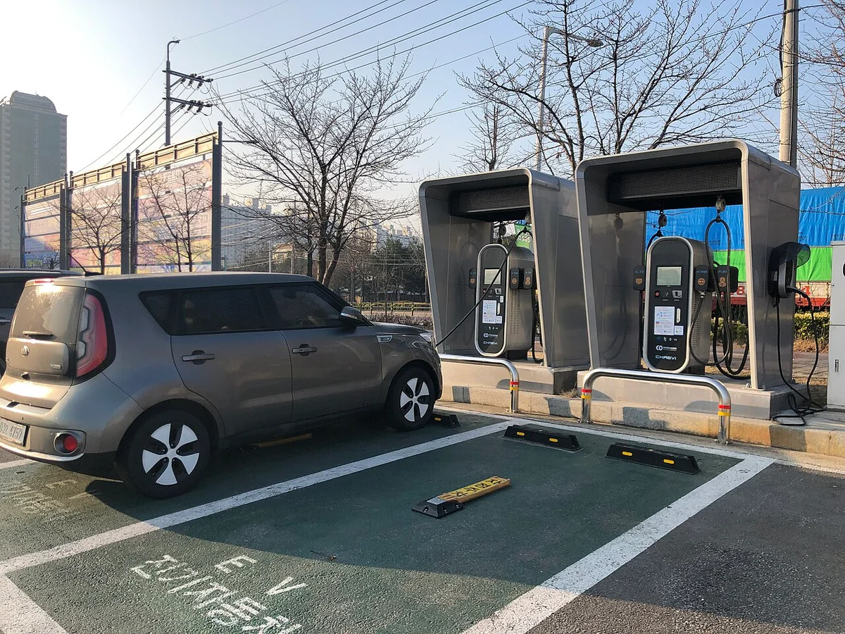 전기차 충전 전용 표시가 있는 초록색 주차구획에 회색 전기차가 서 있고 뒤에 지붕형 충전기 두 대가 설치된 모습