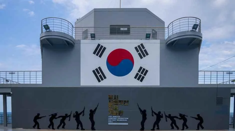 대형 태극기가 걸린 건물 벽과 앞쪽 갑판의 병사 실루엣 그림