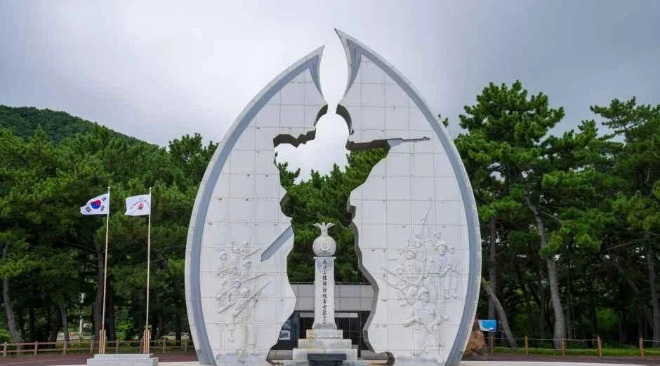 양쪽으로 갈라진 흰 조형물 가운데 작은 탑이 선 기념공원
