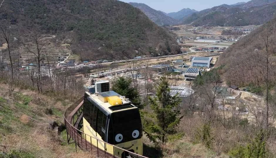 산비탈 궤도를 따라 오르는 소형 차량과 아래로 펼쳐진 산골 마을