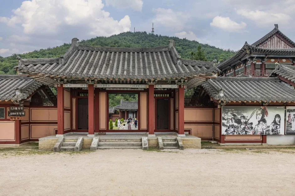 붉은 기둥의 한옥 정문과 기와지붕, 벽화가 그려진 담이 보이는 사극 촬영지 건물