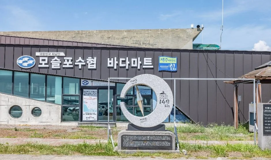 모슬포수협 바다마트 간판과 둥근 기념 조형물이 있는 건물 앞
