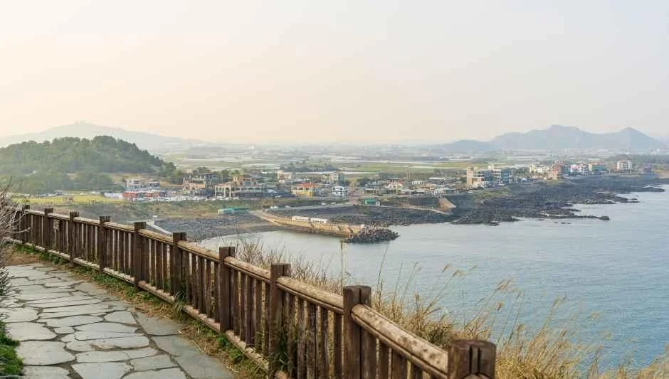 난간을 따라 이어지는 포장 산책로 너머로 마을과 바다가 보이는 풍경