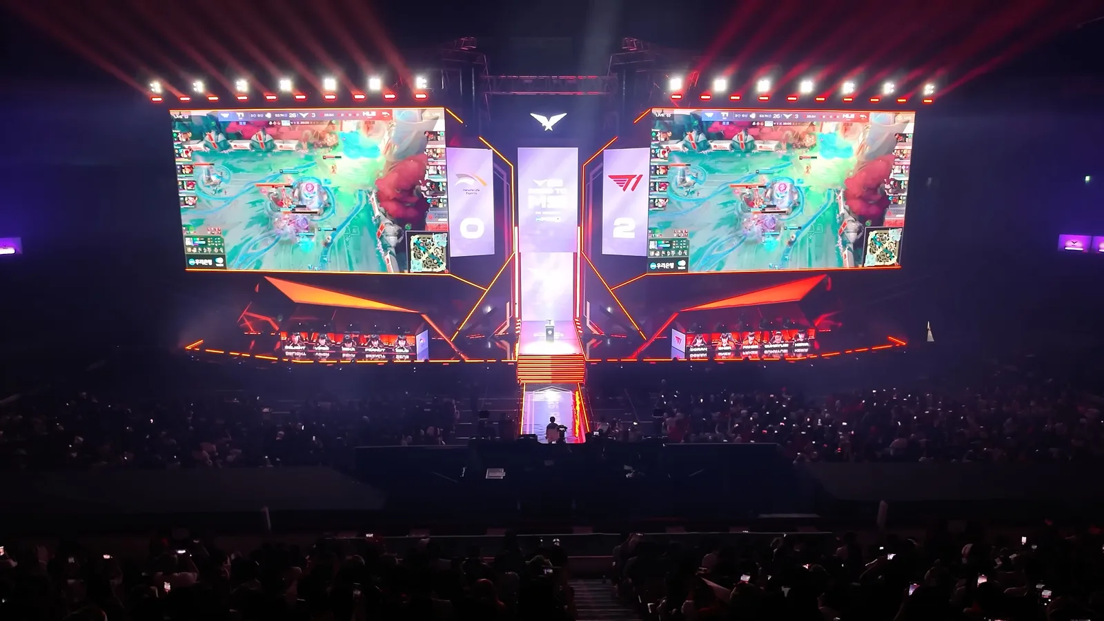 붉은 조명과 대형 LED 스크린이 양옆에 놓인 LCK 대회 무대, 관중석 앞에서 두 팀 선수들이 경기를 치르는 전경