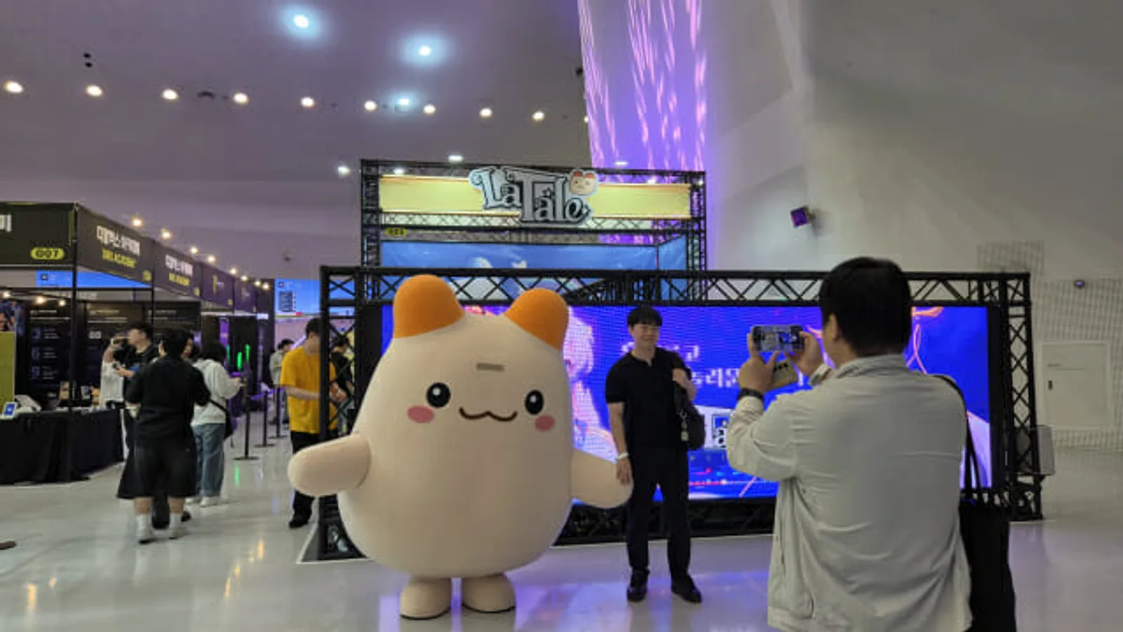 GES 2026 레이싱 게임 부스 사진 - 대형 노란색 부스 구조물 아래 여러 레이싱 시뮬레이터 좌석이 늘어선 모습, 관람객들이 체험을 위해 줄지어 있음