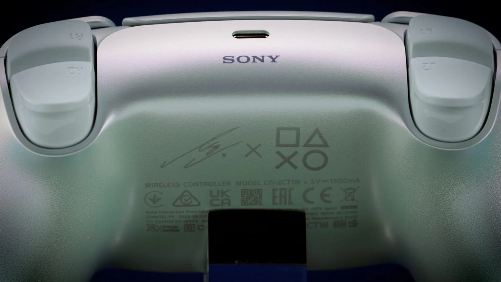 듀얼센스 리사 한정판 후면 클로즈업, SONY 로고와 리사의 사인, 플레이스테이션 버튼 아이콘이 새겨진 뒷판이 보인다
