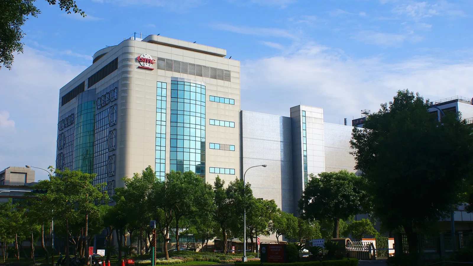 파란 하늘 아래 'tsmc' 로고가 붙은 대만 TSMC 공장 건물, 앞쪽에 나무와 정원이 보인다
