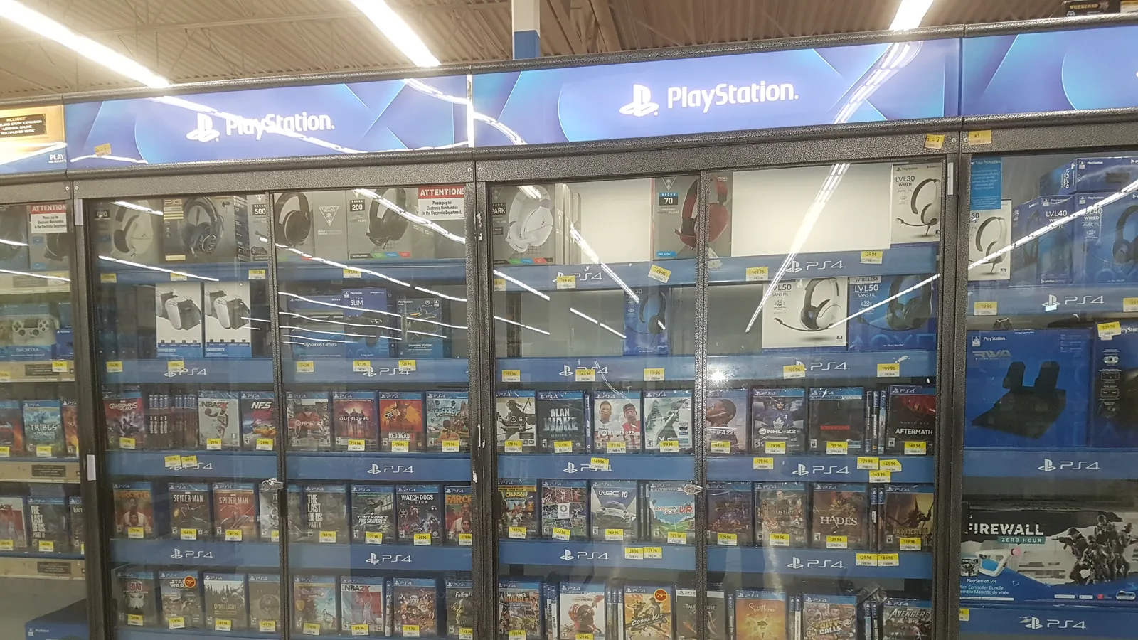 대형 마트 진열장에 PS4 표시가 붙은 칸마다 게임 디스크 패키지와 헤드셋, 컨트롤러가 진열된 모습
