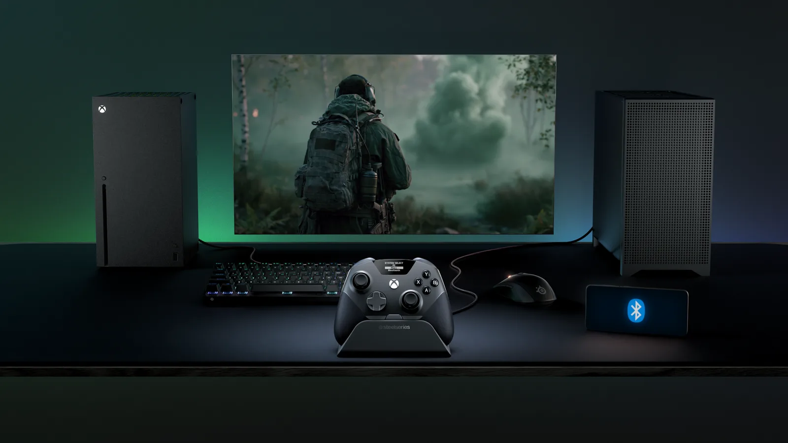 책상 위 모니터 앞 도크에 이온 프로가 세워져 있고, 왼쪽에는 Xbox 시리즈 X, 오른쪽에는 PC 본체와 블루투스 표시가 뜬 스마트폰이 놓여 있다